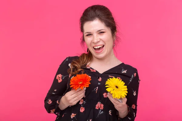 Summer, flowers, funny and people concept - woman having fun with gerberas over the pink background