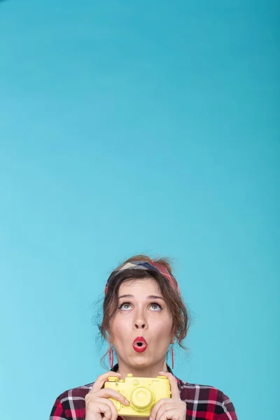 Positive beautiful young woman in retro style holding a yellow film camera in her hands and looking up. Concept space for advertising and information from above.