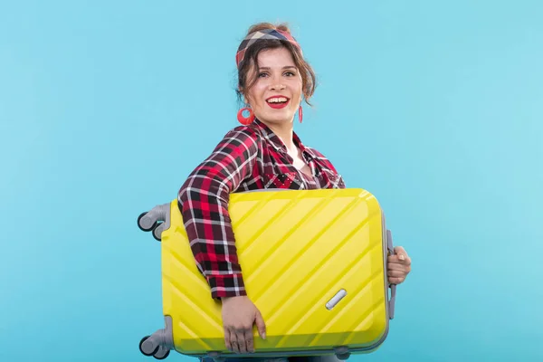Jeune femme souriante positive dans une chemise à carreaux tenant une valise jaune posant sur un fond bleu. Concept de tourisme et de voyage — Photo