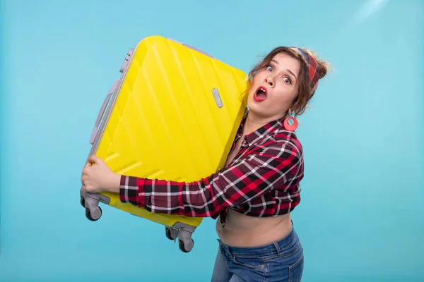 Mavi bir arka plan üzerinde poz elinde sarı bir bavul tutan vintage giysiler içinde korkmuş genç güzel kadın. Ağır yük ile konsept seyahat. — Stok fotoğraf