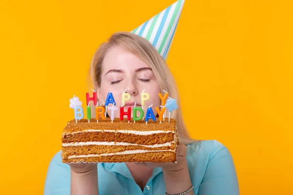 Close-up de engraçado positivo jovem mulher segura em suas mãos um bolo caseiro com a inscrição feliz aniversário posando em um fundo amarelo. Conceito de feriados e aniversários . — Fotografia de Stock