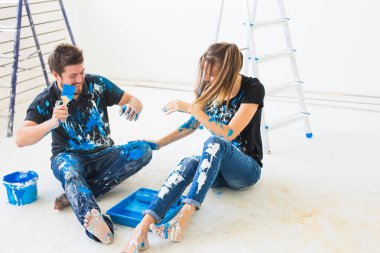 Renovasyon, yeniden dekorasyon ve iç konsept-beyaz katta oturan genç çift ve boya dökmek ve eğlenmek