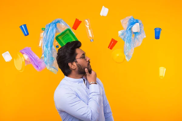 Día Mundial del Medio Ambiente, problema de reciclaje de plástico y concepto de desastre ambiental - Hombre indio serio mirando la basura en el fondo amarillo. Está pensando en reciclar basura. — Foto de Stock