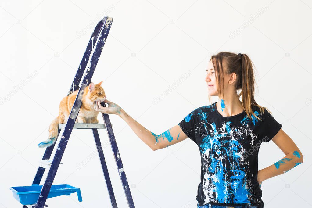 Young woman painter stroking a cat, designer and worker paints the wall. The pet sits next on the ladder and looks at the work.