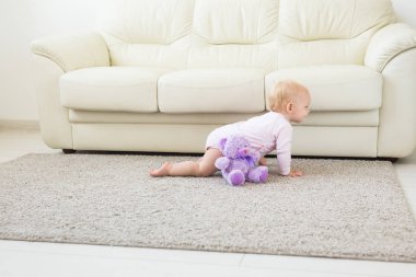 Küçük emekleme kız kız bir yaşında parlak ışık oturma odasında katta sürünerek gülümseyerek ve gülüyor. Evde oynayan mutlu bir çocuk. Çocukluk kavramı