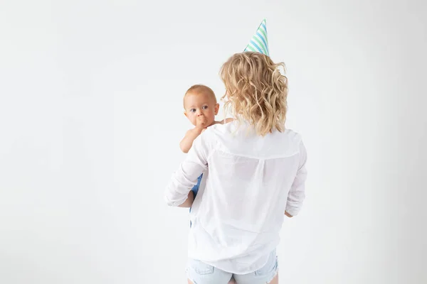 Concepto de familia, maternidad y familia: madre joven con gorra de cumpleaños que sostiene a su bebé sobre un fondo blanco con espacio para copiar — Foto de Stock