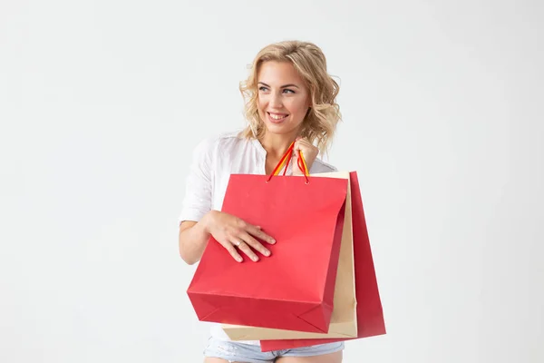 Affascinante giovane donna bionda gioiosa tiene tra le mani borse con un nuovo abbigliamento in posa su uno sfondo bianco. Concetto shopping . — Foto Stock