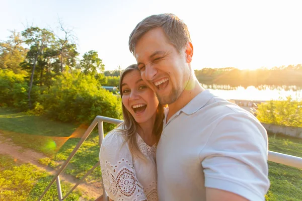 Capturar momentos brilhantes. Joyful jovem engraçado casal amoroso fazendo selfie na câmera enquanto está de pé ao ar livre — Fotografia de Stock