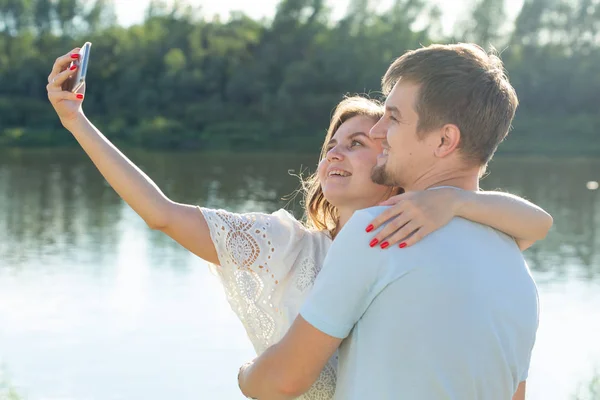 Belo casal romântico no fundo da natureza. Jovem atraente e homem bonito estão fazendo selfie, sorrindo e olhando para a câmera . — Fotografia de Stock