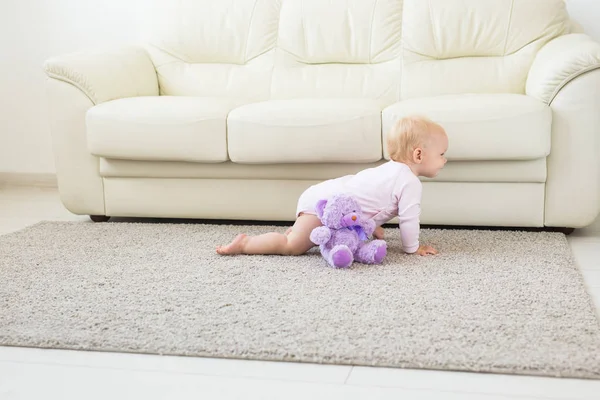 Küçük emekleme kız kız bir yaşında parlak ışık oturma odasında katta sürünerek gülümseyerek ve gülüyor. Evde oynayan mutlu bir çocuk. Çocukluk kavramı
