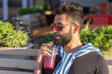 Sıcak güneşli bir yaz gününde parkta yürürken bir saman ile meyve suyu bir bardak ile olumlu neşeli bir genç adam Portresi. Çalışma sonrası dinlenme kavramı ve hafta sonları çalışma.