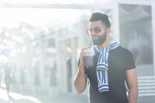 Lindo estilo árabe joven hipster masculino con un bigote y una barba y el uso de gafas de beber jugo con una paja. Concepto vacaciones de verano . — Foto de Stock