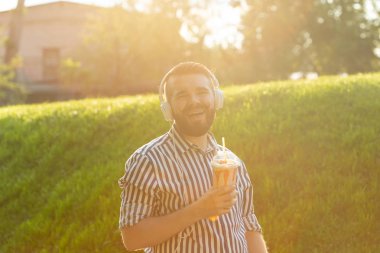 Sakallı, süt sallama lı ve sıcak bir yaz gününde parkta yürüyen şehrin manzarasına hayran olan şık bir genç adamın yan görünümü. Dinlenme ve rahatlama kavramı.