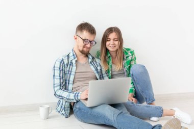 Casual giysi Charming genç olumlu çift bir dizüstü bilgisayar ve yüksek hızlı Internet kullanarak yeni daire için bir iç tasarımcı arıyor. Daire tasarım konsepti.