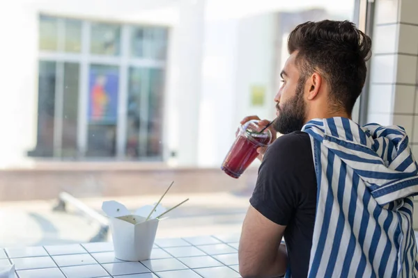 Позитивный молодой стильный парень пьет сок в кафе во время перерыва на работе. Концепция отдыха и здоровых закусок . — стоковое фото