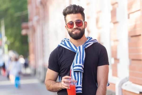 Lindo estilo árabe joven hipster masculino con un bigote y una barba y el uso de gafas de beber jugo con una paja. Concepto vacaciones de verano . — Foto de Stock