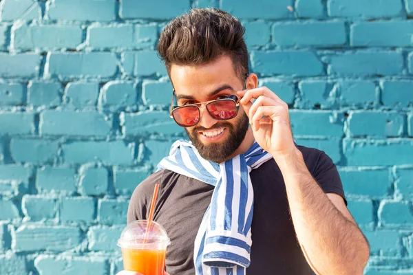 Lindo estilo árabe joven hipster masculino con un bigote y una barba y el uso de gafas de beber jugo con una paja. Concepto vacaciones de verano . — Foto de Stock