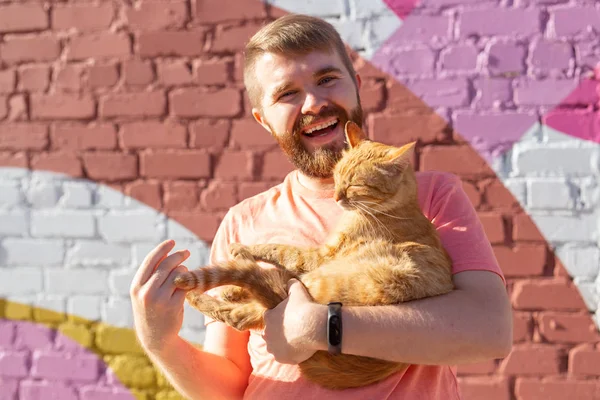 Handsome man is holding and hugging cute cat outdoors — Stock Photo, Image