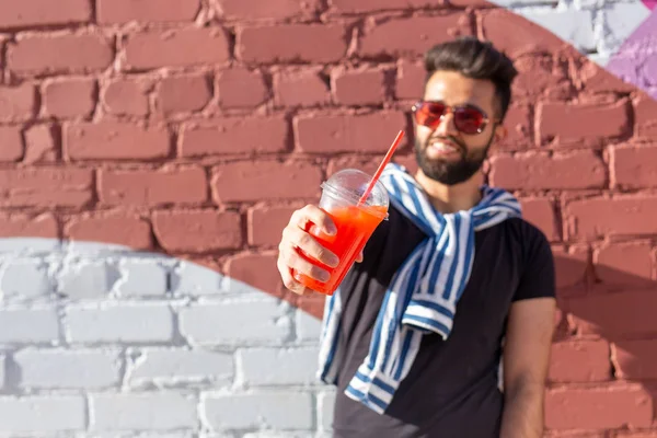 Retrato de un joven árabe alegre positivo con un vaso de jugo con una pajita mientras camina por la ciudad en un cálido día soleado de verano. El concepto de descanso después del estudio y el trabajo los fines de semana . — Foto de Stock