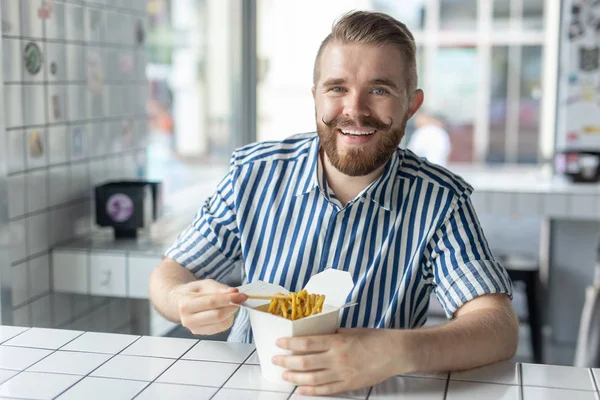 직장에서 휴식을 취하는 동안 카페에서 중국 국수를 먹는 긍정적 인 젊은 세련된 남자. 휴식과 건강한 간식의 개념. — 스톡 사진