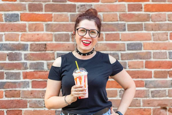 Чарівна весела молода стильна дівчина тримає молочний коктейль з соломою на фоні цегляної стіни. Концепція літнього відпочинку в кафе і на вулиці . — стокове фото