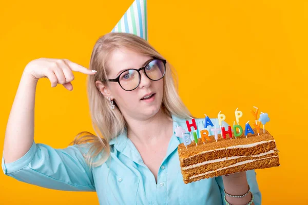 Zabawna pozytywna młoda kobieta trzyma w dłoniach domowy tort z napisem Happy Birthday stwarzających na żółtym tle. Koncepcja świąt i rocznic. — Zdjęcie stockowe