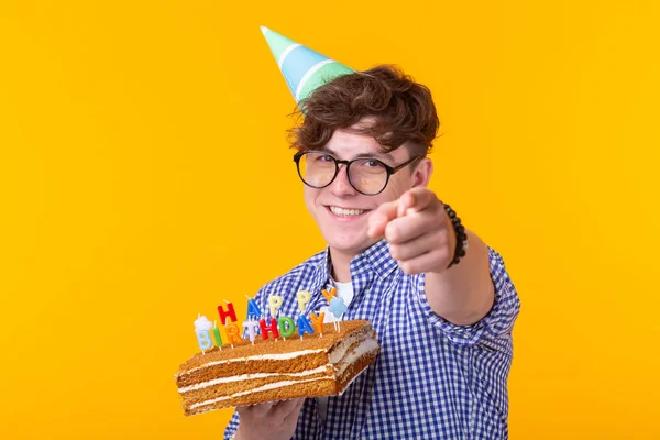 Pozytywny młody człowiek trzyma szczęśliwy tort urodzinowy pozowanie na żółtym tle. — Zdjęcie stockowe