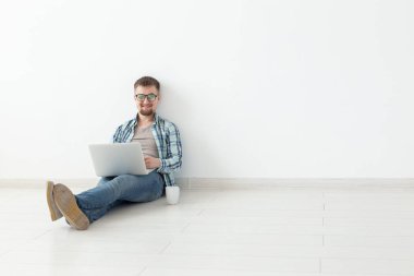 Boş bir odada yerde oturan yeni konut arayışı içinde Internette sörf Casual giysiler olumlu genç adam. Internet ve dizüstü bilgisayar kullanarak bir daire bulma kavramı. Boşaltmak