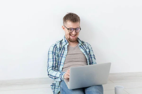 Joven positivo en ropa casual navegando por Internet en busca de una nueva vivienda sentada en el suelo en una habitación vacía con espacio para copias — Foto de Stock