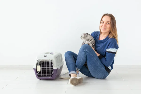 Encantadora joven positiva sostiene en sus manos a su hermoso gato escocés gris plegado sentado en el suelo en un nuevo apartamento. Concepto de mascota . — Foto de Stock