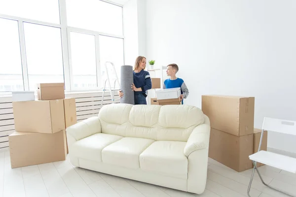 Young cute single mother and son are happy about the move to new house holding a pot of greens and carpet in their hands. Concept of housewarming and family space extensions. — Stock Photo, Image