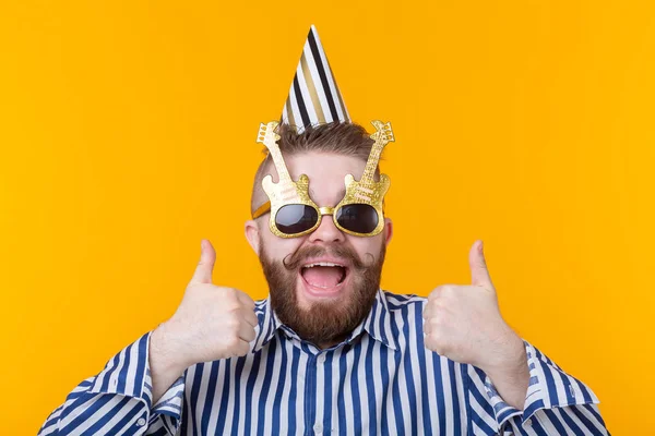 Loco joven hipster positivo chico con una barba se ríe felizmente sobre un fondo amarillo. El concepto de vacaciones y ventas — Foto de Stock