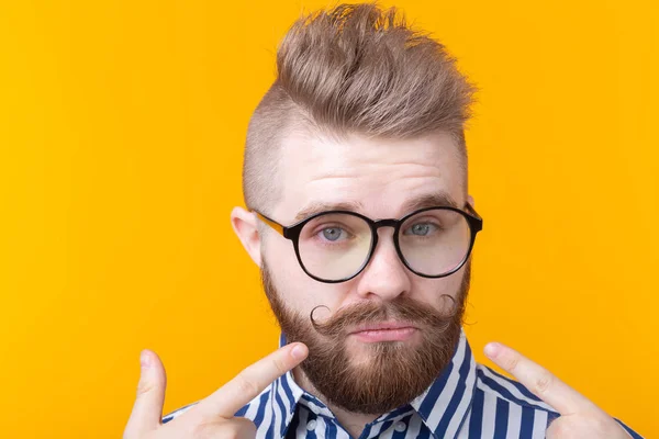 Encantador joven hombre hipster de moda con gafas y una barba se muestra posando sobre un fondo amarillo. Lugar para la publicidad. El concepto de confianza en sí mismo y éxito . — Foto de Stock