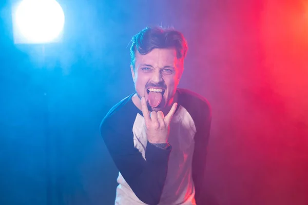 Hombre excitado pegando la lengua y mostrando un gesto de rock and roll. Retrato de un fanático del rock masculino mostrando un signo de cuerno. Concepto de ventilador — Foto de Stock