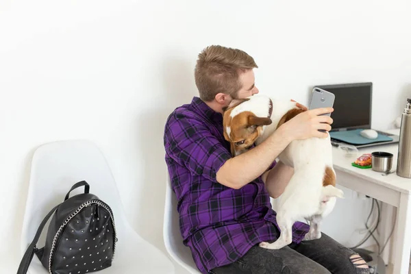 people, pets and animals concept - young man hugging jack russell terrier and trying to work