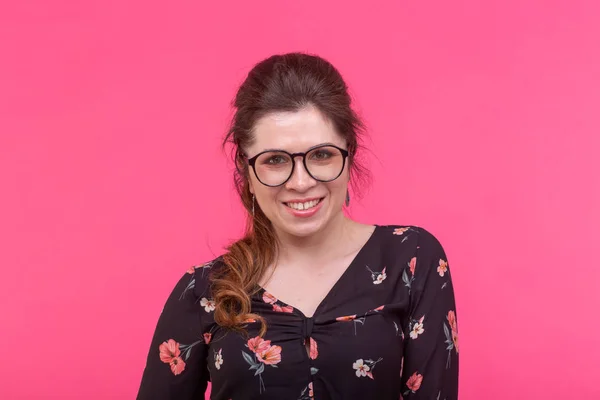 Portrait d'une jeune femme intelligente et charmante aux yeux bruns aux lunettes posant sur un fond rose vif — Photo
