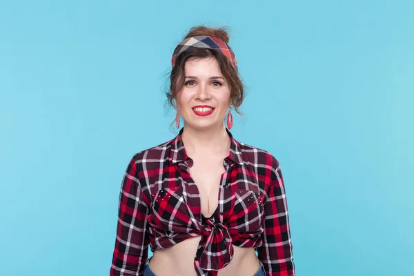 Mujer joven hermosa positiva en una camisa vintage a cuadros mirando a la cámara y posando sonriente sobre un fondo azul . — Foto de Stock