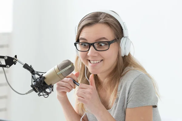 Radio host concept - Funny woman working as radio host sitting in front of microphone over white background in studio — Stock Photo, Image