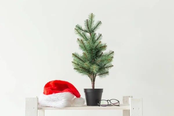 Kutlama, kış tatilleri ve reklam konsepti - beyaz arka plan üzerinde küçük noel ağacı ve santa şapka — Stok fotoğraf