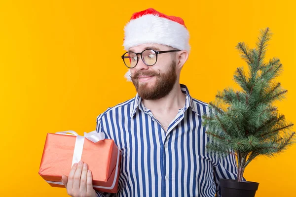 Joven positivo Santa Claus con regalos y árbol de Navidad posando sobre un fondo amarillo. Navidad y Año Nuevo concepto de vacaciones . — Foto de Stock