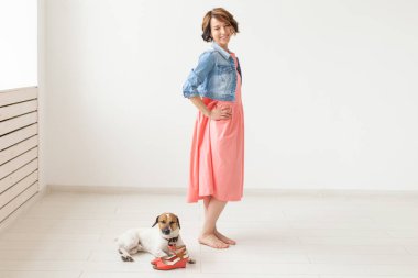 Uzun bir elbise ve beyaz bir arka plan üzerinde poz sevgili köpek ile denim elbise genç neşeli kadın. Günlük giyim kavramı.
