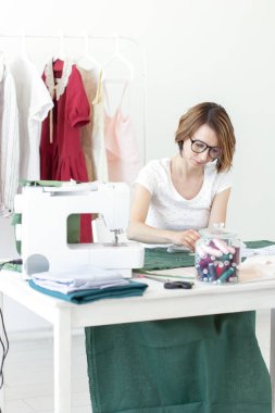 Üniversitede bir giysi tasarımcısı genç güzel kız öğrenci çalışma ve bir dikiş makinesi ile bir masada oturan ilk tezyapar. Giyim tasarım konsepti.