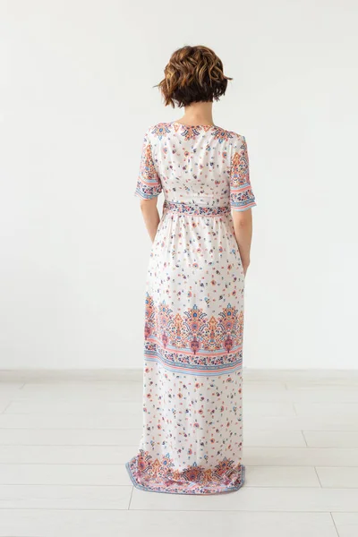 Achteraanzicht van een jonge slanke vrouw in een jurk met lange motieven die tegen een witte muur staat. Het concept van unieke producten om te bestellen — Stockfoto