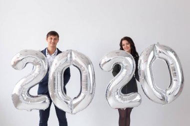 Yeni yıl, kutlama ve tatil konsepti - beyaz arka plan üzerinde yeni yıl için gümüş balonlardan yapılmış 2020 işareti ile eğlenen aşk çift