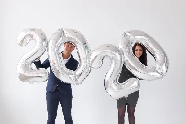 Año nuevo, celebración y concepto de vacaciones - pareja de amor divirtiéndose con signo 2020 hecho de globos de plata para el año nuevo sobre fondo blanco — Foto de Stock