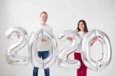 Yeni yıl, kutlama ve tatil konsepti - beyaz arka plan üzerinde yeni yıl için gümüş balonlardan yapılmış 2020 işareti ile eğlenen aşk çift