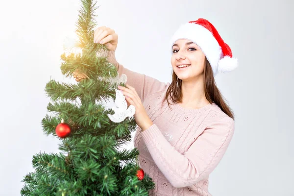 Holidays and celebration concept - Happy brunette woman in santas hat decorates a christmas tree at home in the living room