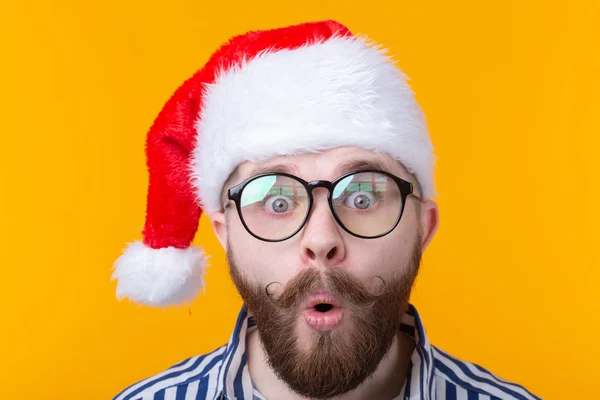 Meglepett fiatalember Santa Claus nézi a kamerát, sárga háttér. A koncepció gratulálok az új évet és karácsonyra. Reklámfelület. — Stock Fotó