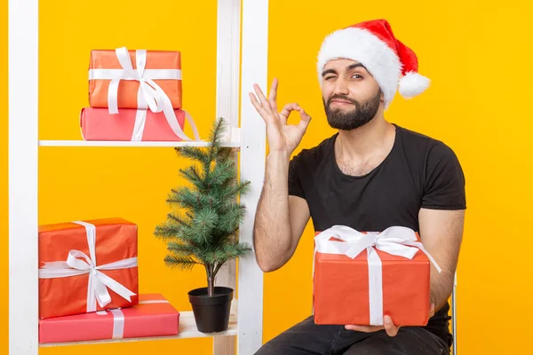 Jeune homme beau dans un chapeau de Père Noël tient cadeaux de félicitations à côté d'un arbre de Noël. Concept de vacances de Noël et du nouvel an . — Photo