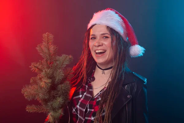 Natal, rock, estúdio, conceito de pessoas - jovem mulher em chapéu de Natal com pequena árvore de Natal sobre o fundo escuro — Fotografia de Stock